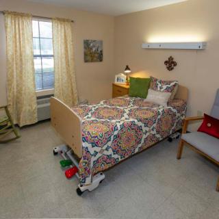 A cozy bedroom with a neatly made single bed, an armchair, and a well-lit window.