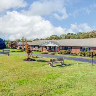 A one-story brick building surrounded by a green lawn and trees under a partly cloudy sky.