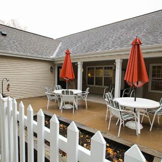 A cozy outdoor patio area with tables, chairs, and red umbrellas surrounded by a white picket fence.