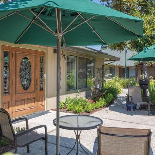A sunny outdoor patio with a table, chairs, and large green umbrellas.