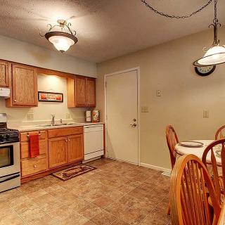 A cozy kitchen and dining area featuring wooden cabinets, a stove, a dishwasher, and a small dining table with chairs.