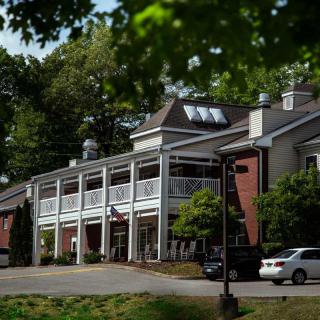 A two-story building surrounded by trees with cars parked in front.