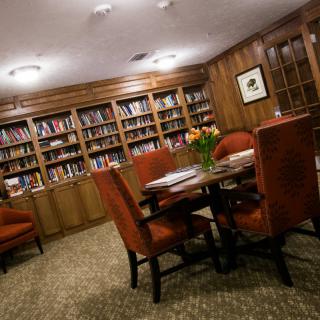 A cozy library room with bookshelves lining the walls, a table surrounded by chairs, and elegant wood paneling.
