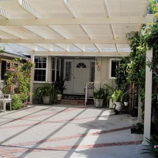A house entrance with a pergola-covered patio adorned with various potted plants.