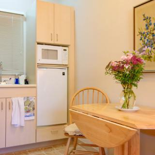 A cozy kitchen with a small dining area, featuring a wooden table with chairs and a vase of flowers.