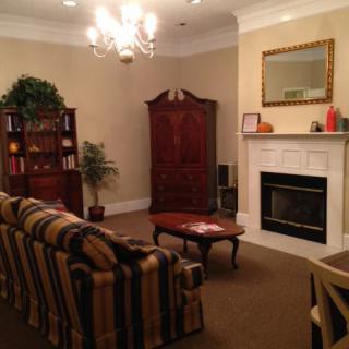 A cozy living room featuring a striped sofa, coffee table, and fireplace setup with a bookshelf and indoor plant in the corner.