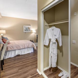 A cozy hotel room with a bed and a closet showcasing a plush robe.