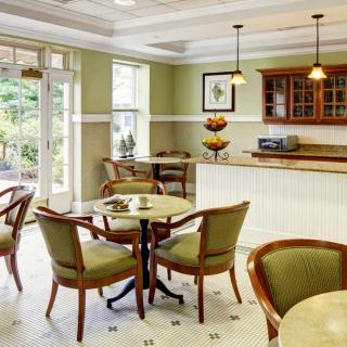 A cozy cafe interior featuring neatly arranged tables and chairs, a serving counter, and warm lighting.