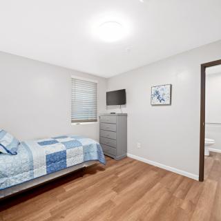 A modern, minimalist bedroom with a single bed, wooden flooring, and wall-mounted TV.