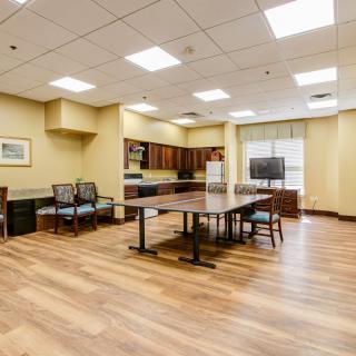 A spacious kitchen and dining area with wooden flooring, featuring a large table, chairs, a television, and ample cabinet space.
