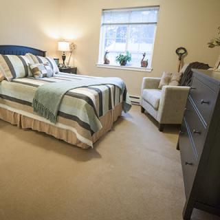 A cozy bedroom with a neatly made bed, a lamp on the bedside table, and a comfortable chair by the window.