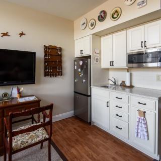 A cozy kitchen and dining area with white cabinets, a mounted television, and decorative plates on the wall.