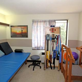 A well-equipped physical therapy room with exercise equipment and a therapy bed.