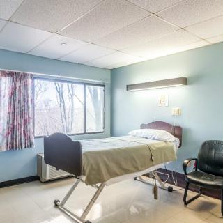 An empty hospital room with a single bed and chair.
