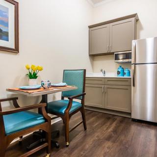 A cozy kitchen and dining area featuring modern appliances, a small table with two chairs, and a vase of yellow flowers.