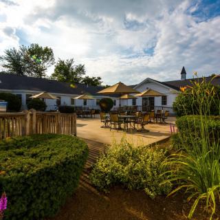 A tranquil garden with outdoor seating and a building in the background under a partly cloudy sky.