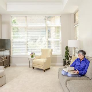 A senior woman reads a book in a cozy, well-lit modern living room.