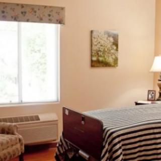 A cozy bedroom with a window, bed, lamp, and chair.
