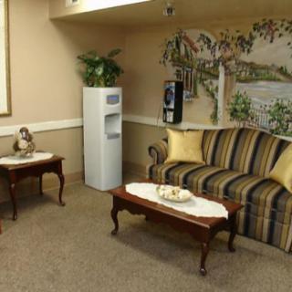 A cozy waiting room featuring a striped sofa, coffee tables with decorative items, and a water cooler.