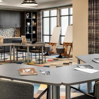 A modern meeting room with angular tables, chairs, and easels, featuring ample natural light and a stylish design.