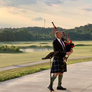 A bagpiper playing outdoors at sunset, wearing a traditional kilt.