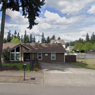 A suburban house with a driveway and trees in the background under a cloudy sky.
