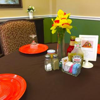A cozy restaurant table set with orange plates, condiments, and a vase of vibrant flowers.