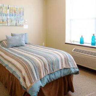A cozy bedroom with a single bed featuring striped bedding, decorative pillows, and a bright window letting in natural light.