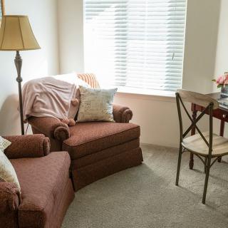 A cozy living room corner with a comfortable chair, lamp, and table near a window.