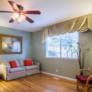 A cozy living room with a couch, an armchair, a ceiling fan, and a window with draped curtains.