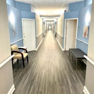 A brightly lit hallway with blue walls, featuring chairs and a bench along the sides.