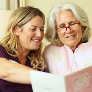 An elderly woman and a younger woman enjoying reading together.