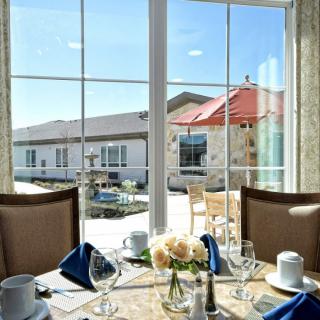 A beautifully set dining table by a window overlooking an outdoor patio on a sunny day.