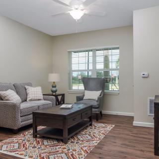 A cozy living room with a sofa, armchair, and coffee table, softly lit by a lamp next to a window.
