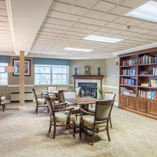 A cozy library interior featuring tables, chairs, a fireplace, and well-stocked bookshelves.