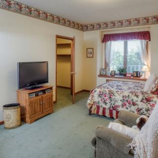 A cozy bedroom with floral bedding, a TV on a stand, and a window with scenic views.