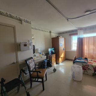 A patient room in a hospital, showcasing the interior layout with furniture and natural light.