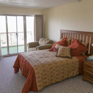 A cozy bedroom with a bed, armchair, and sliding glass doors leading to a balcony.