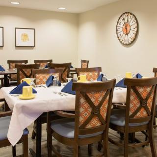 A well-arranged dining room with neatly set tables, featuring blue and yellow napkins and a large wall clock.