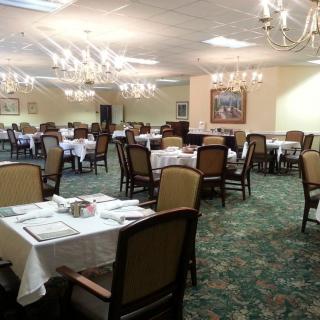 An elegant dining room with neatly arranged tables and chairs, lit by chandeliers.