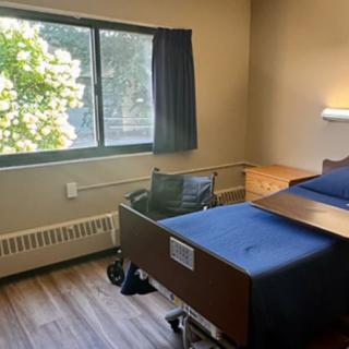 A hospital room with a bed, wheelchair, and window with curtains.