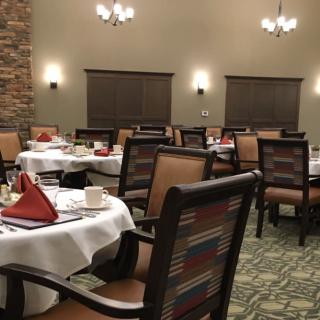 A neatly arranged dining room with tables set for guests, featuring comfortable chairs and elegant lighting.
