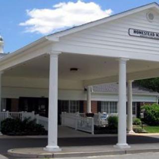 A building with a covered entrance featuring white columns and a roof.