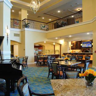 A spacious, elegantly decorated lobby with dining tables and a grand piano.