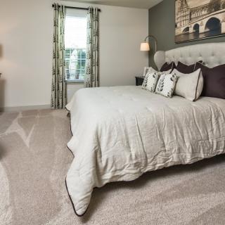 A modern bedroom with stylish dcor, featuring a plush bed, carpeted flooring, and elegant artwork on the wall.