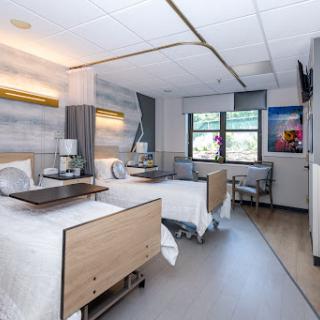 A modern hospital patient room featuring two beds, equipped with bedside tables and ample natural light.