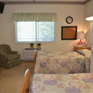 A cozy bedroom with twin beds featuring floral bedspreads, an armchair by the window, and a bedside lamp providing soft lighting.