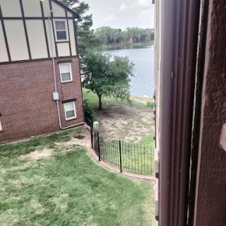 A view from an apartment window overlooking a serene lake and green lawn.