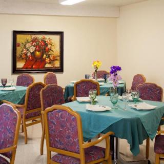 A dining room with neatly set tables and a floral painting on the wall.