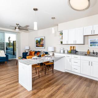 A modern open-plan kitchen and living room with white cabinets and wood flooring.